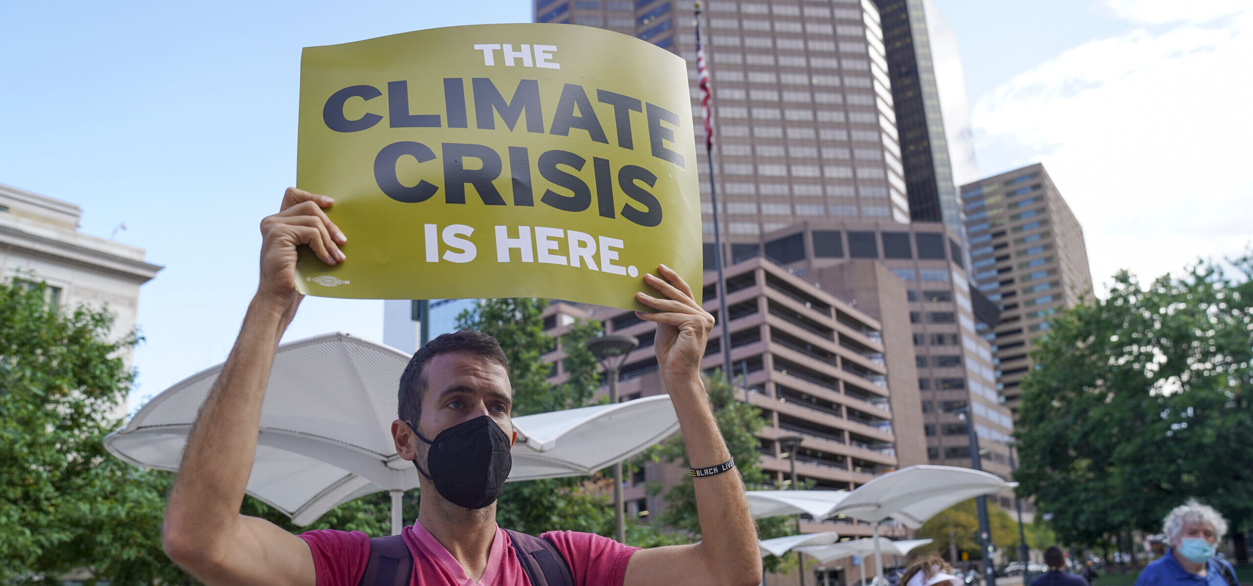 A Colorado Green New Deal organizer holds up a “Climate crisis is here” sign at a rally